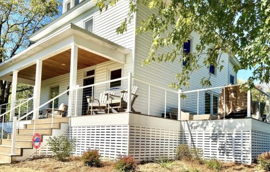Finished covered deck with cable railing, wood plank ceiling, and white skirting on a two story home